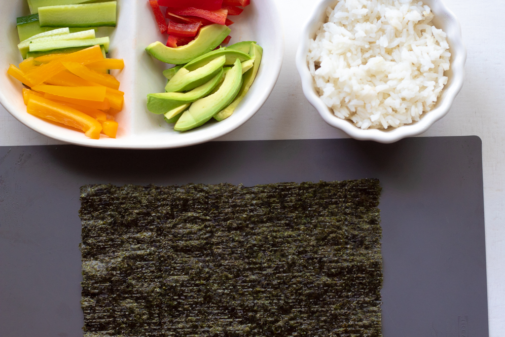 Nori sheet and a small bowl of rice and a platter of cut vegetables