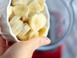 Someone adding bananas to a blender