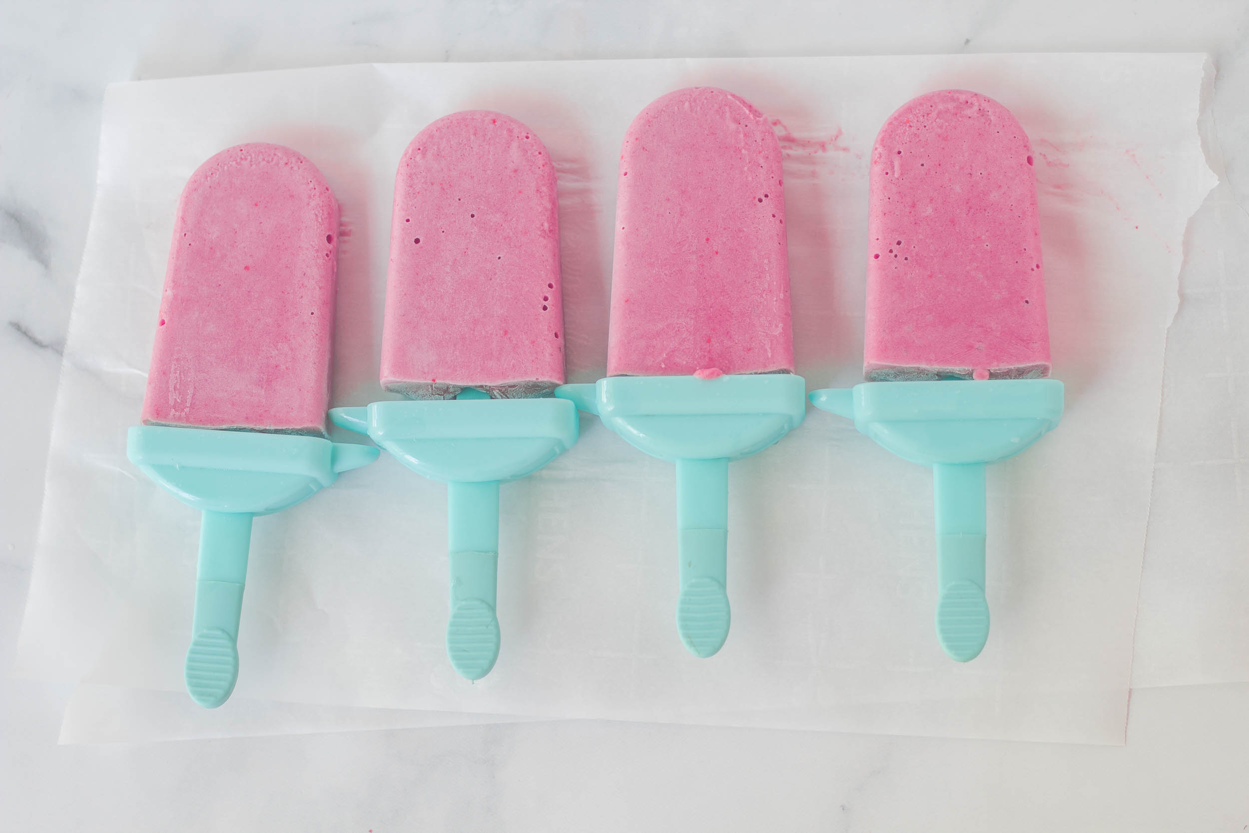 4 strawberry banana cream popsicles on parchment paper