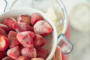 Someone adding strawberries to the blender